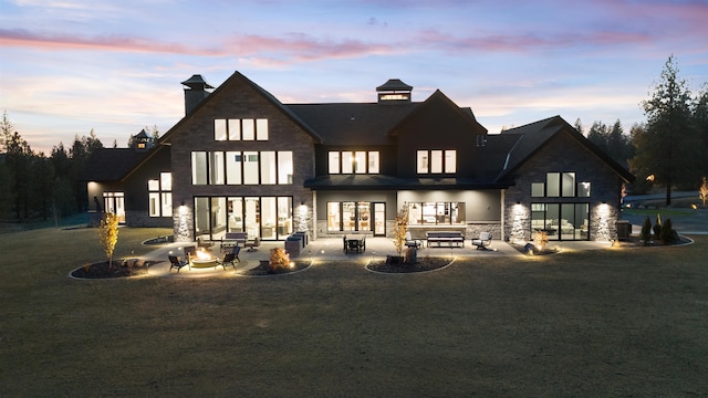 back house at dusk featuring a patio area, a lawn, and a fire pit