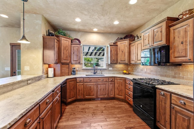 kitchen featuring hanging light fixtures, light hardwood / wood-style floors, black appliances, backsplash, and sink