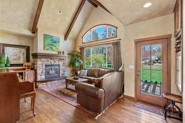 living room with light hardwood / wood-style floors, a stone fireplace, high vaulted ceiling, and beam ceiling