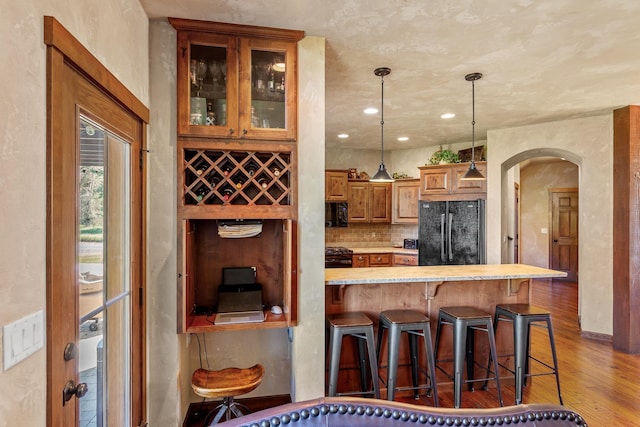 kitchen featuring hardwood / wood-style flooring, decorative light fixtures, black appliances, decorative backsplash, and a kitchen bar