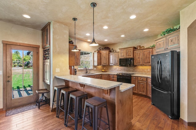 kitchen featuring sink, kitchen peninsula, a breakfast bar area, wood-type flooring, and black appliances