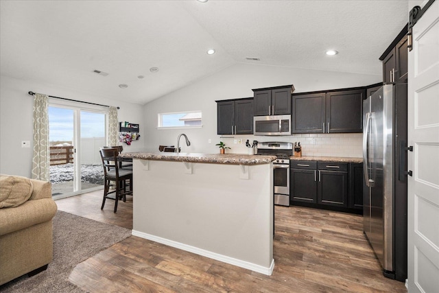 kitchen with a kitchen breakfast bar, a barn door, appliances with stainless steel finishes, an island with sink, and dark hardwood / wood-style flooring