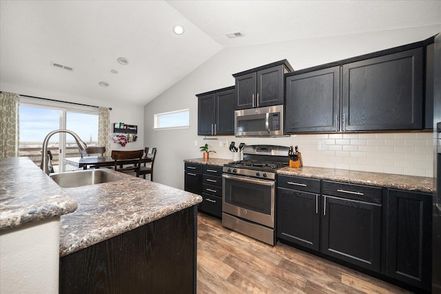 kitchen featuring vaulted ceiling, appliances with stainless steel finishes, hardwood / wood-style flooring, sink, and tasteful backsplash