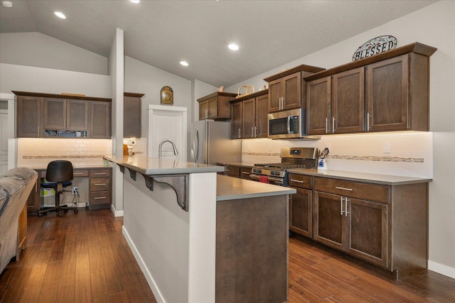 kitchen with a breakfast bar, lofted ceiling, a kitchen island with sink, backsplash, and appliances with stainless steel finishes