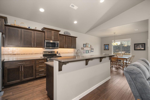 kitchen featuring vaulted ceiling, a breakfast bar area, appliances with stainless steel finishes, dark hardwood / wood-style flooring, and pendant lighting