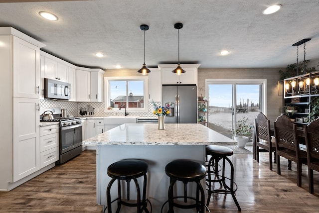 kitchen with white cabinets, appliances with stainless steel finishes, pendant lighting, and a center island