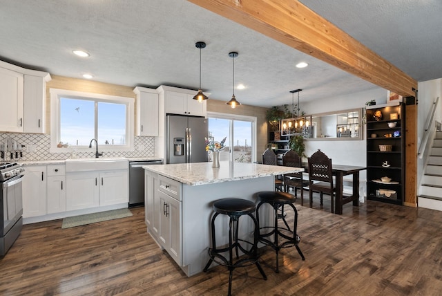 kitchen with stainless steel appliances, a kitchen island, white cabinetry, and pendant lighting