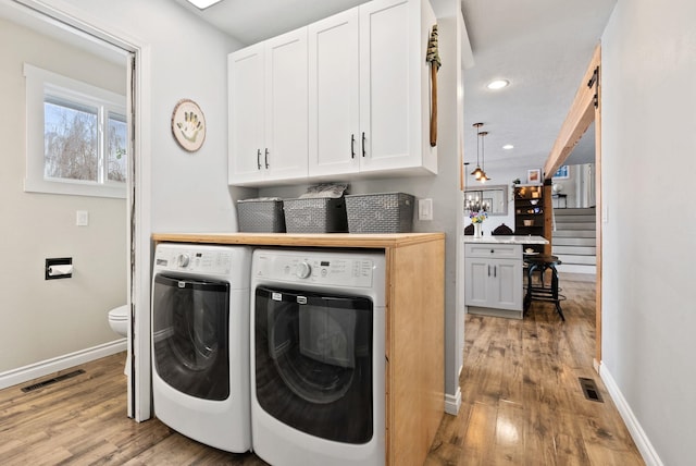 clothes washing area with light hardwood / wood-style floors, cabinets, and independent washer and dryer