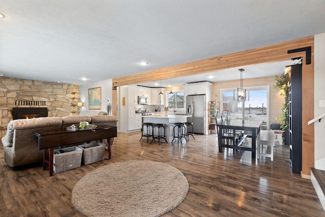 living room featuring sink, dark hardwood / wood-style flooring, beamed ceiling, and a stone fireplace