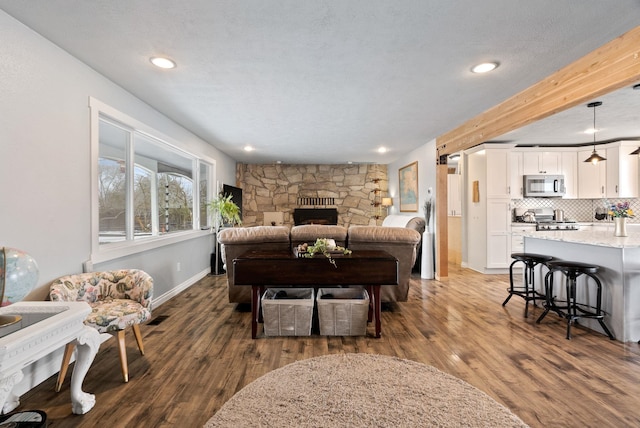 living room with dark hardwood / wood-style flooring, a fireplace, a textured ceiling, and beamed ceiling