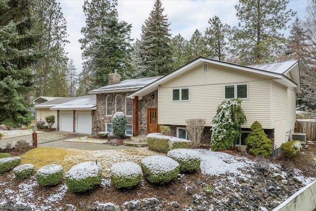 bi-level home featuring a garage, stone siding, a chimney, and central air condition unit