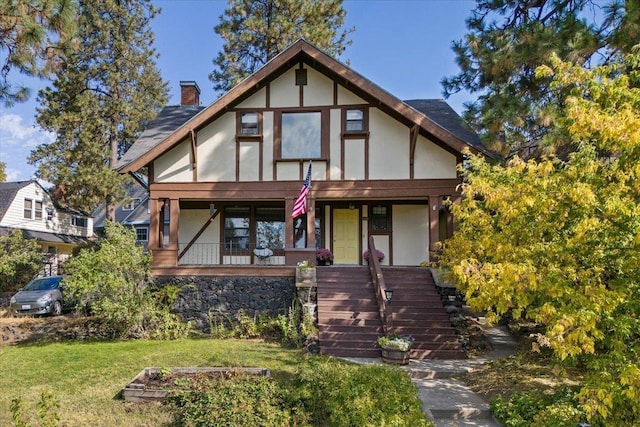 english style home with covered porch and a front yard