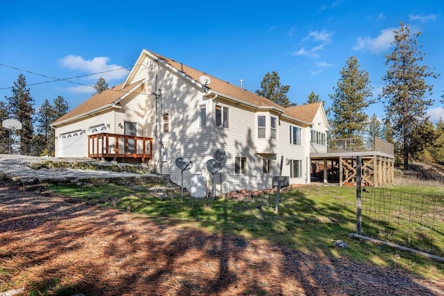 back of property featuring a lawn, a garage, and a wooden deck