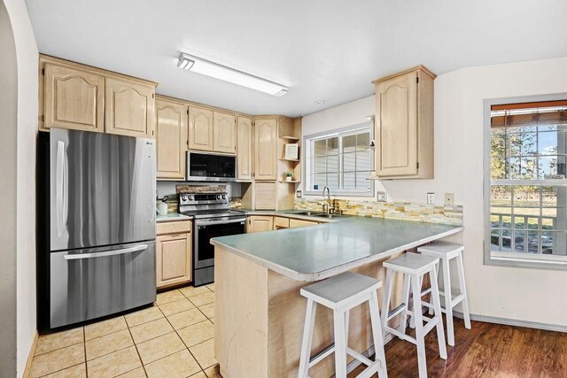 kitchen with sink, stainless steel appliances, light brown cabinetry, and kitchen peninsula