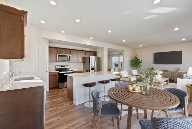 kitchen featuring hardwood / wood-style floors, a breakfast bar area, appliances with stainless steel finishes, a kitchen island, and sink