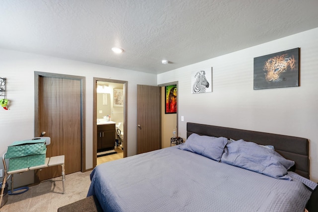 carpeted bedroom with ensuite bathroom and a textured ceiling