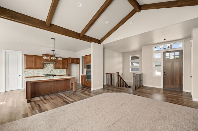 kitchen featuring sink, tasteful backsplash, decorative light fixtures, and a center island with sink