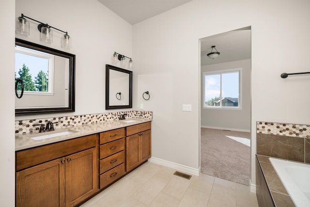 bathroom with vanity, tile patterned flooring, a relaxing tiled tub, and backsplash