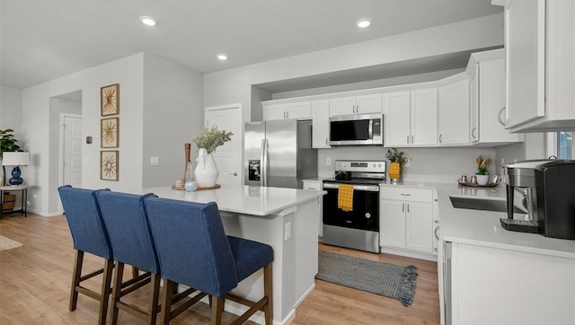 kitchen featuring stainless steel appliances, light hardwood / wood-style floors, a kitchen bar, and white cabinetry