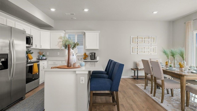 kitchen with a center island, stainless steel appliances, a breakfast bar, light wood-type flooring, and white cabinets