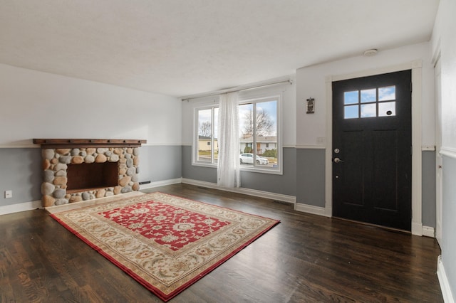 entryway with dark hardwood / wood-style flooring and a stone fireplace