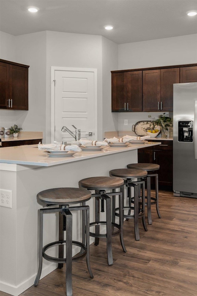 kitchen featuring dark wood-type flooring, stainless steel fridge, dark brown cabinets, and a breakfast bar area