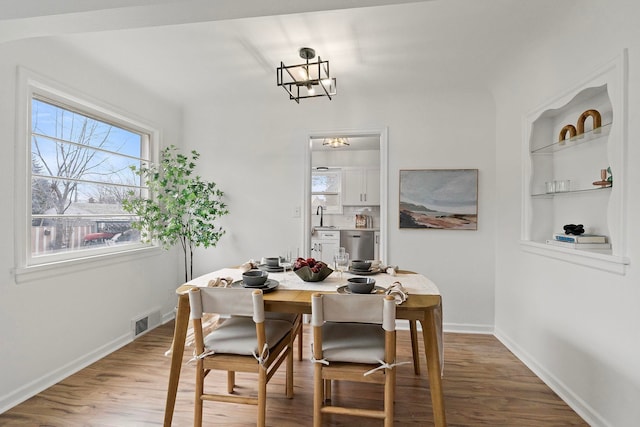 dining area with hardwood / wood-style floors, built in features, a chandelier, and sink