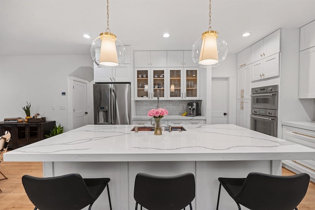 kitchen featuring stainless steel appliances, a kitchen island with sink, backsplash, and white cabinetry