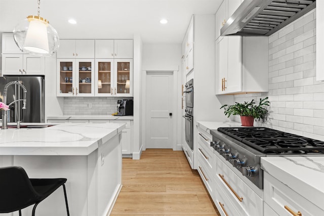 kitchen with stainless steel appliances, white cabinets, light stone counters, wall chimney exhaust hood, and decorative backsplash