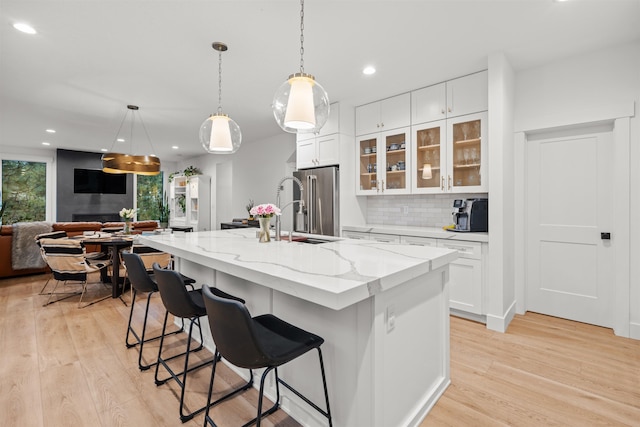 kitchen featuring light stone countertops, a kitchen island with sink, backsplash, white cabinetry, and high end fridge