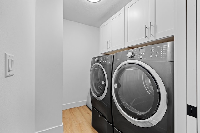 laundry area with light wood-type flooring, cabinets, washing machine and clothes dryer, and a textured ceiling