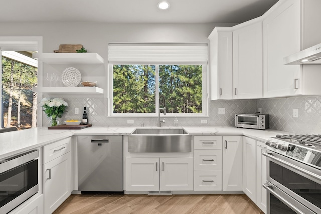 kitchen featuring white cabinetry, appliances with stainless steel finishes, backsplash, light stone countertops, and sink