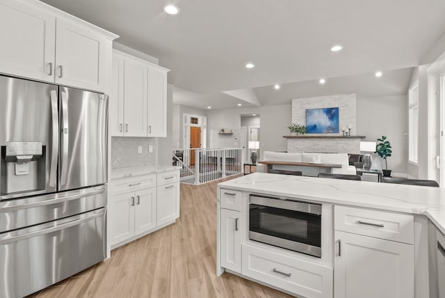 kitchen featuring stainless steel refrigerator with ice dispenser, backsplash, white cabinets, built in microwave, and light stone counters