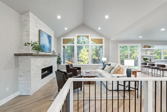 living room featuring vaulted ceiling, light hardwood / wood-style floors, and a stone fireplace