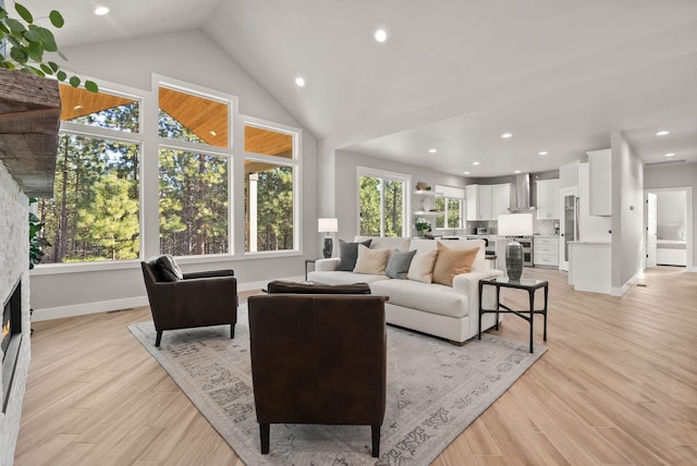 living room featuring light wood-type flooring, a wealth of natural light, a fireplace, and high vaulted ceiling