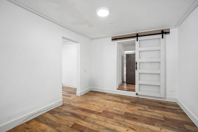 empty room featuring built in shelves, crown molding, a barn door, and dark hardwood / wood-style floors