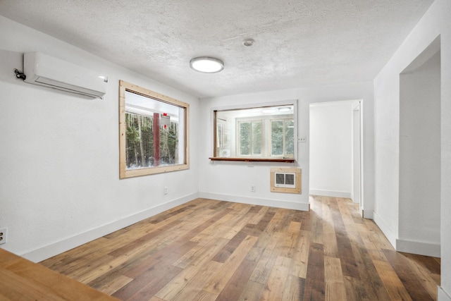 spare room featuring a textured ceiling, a wall unit AC, wood-type flooring, and heating unit