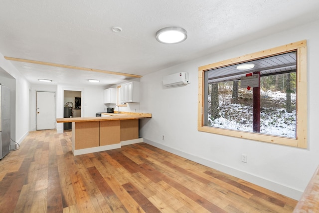 kitchen with a wall unit AC, kitchen peninsula, a kitchen bar, white cabinets, and light hardwood / wood-style flooring