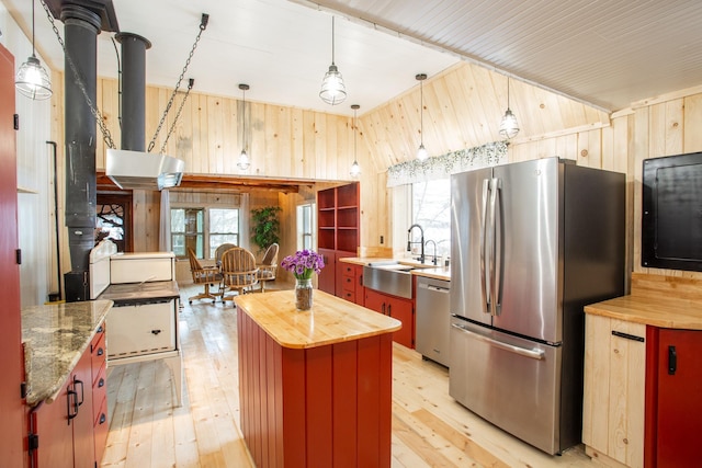 kitchen with wood walls, a center island, butcher block countertops, sink, and stainless steel appliances