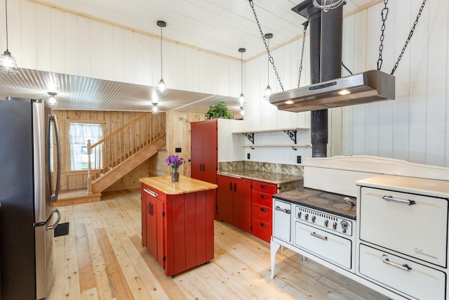 kitchen with wood walls, butcher block countertops, light wood-type flooring, stainless steel refrigerator, and range hood