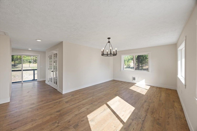 empty room featuring a wealth of natural light, dark hardwood / wood-style flooring, and a chandelier