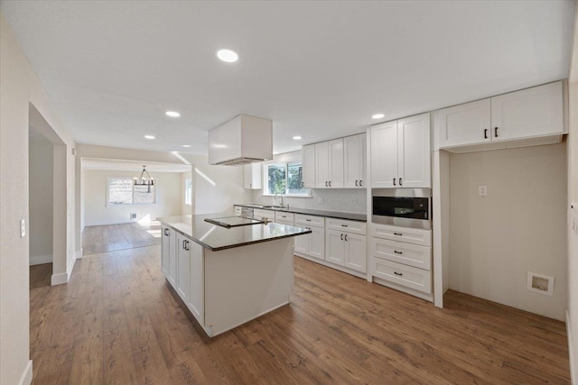 kitchen with black electric cooktop, hardwood / wood-style flooring, white cabinetry, and built in microwave