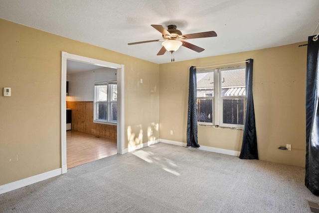 empty room with light carpet, ceiling fan, a wealth of natural light, and wooden walls