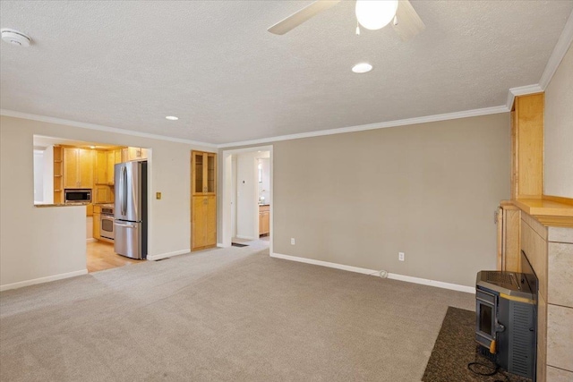 unfurnished living room with ceiling fan, a wood stove, light carpet, and ornamental molding