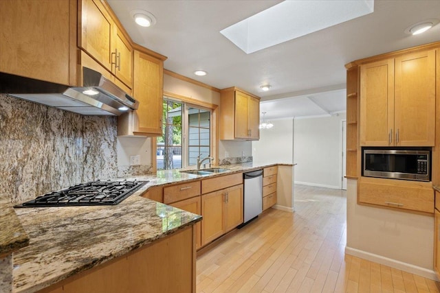 kitchen with appliances with stainless steel finishes, a skylight, decorative backsplash, sink, and light stone counters