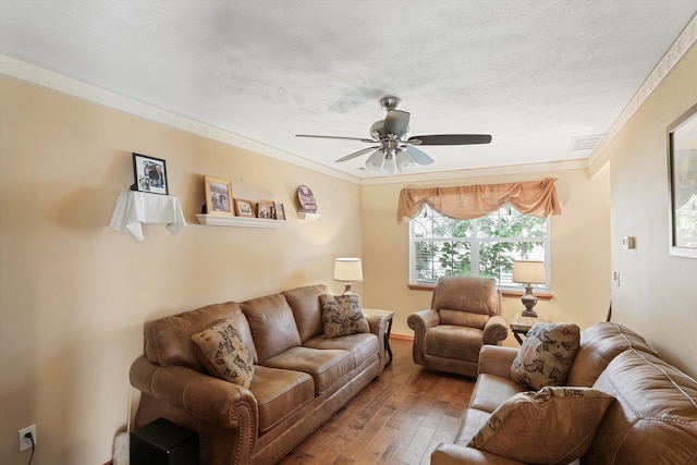 living room featuring ceiling fan, wood-type flooring, ornamental molding, and a textured ceiling