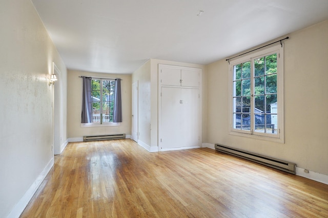 unfurnished bedroom with a baseboard heating unit, light wood-type flooring, and multiple windows