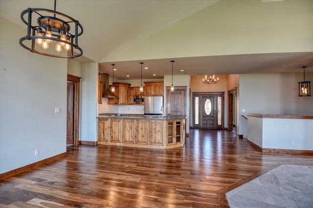 kitchen with wall chimney exhaust hood, decorative light fixtures, stainless steel appliances, a chandelier, and high vaulted ceiling