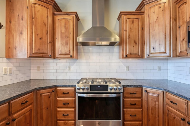 kitchen featuring decorative backsplash, dark stone counters, wall chimney range hood, and stainless steel range with gas cooktop