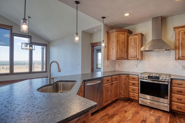 kitchen with appliances with stainless steel finishes, decorative light fixtures, lofted ceiling, wall chimney exhaust hood, and sink